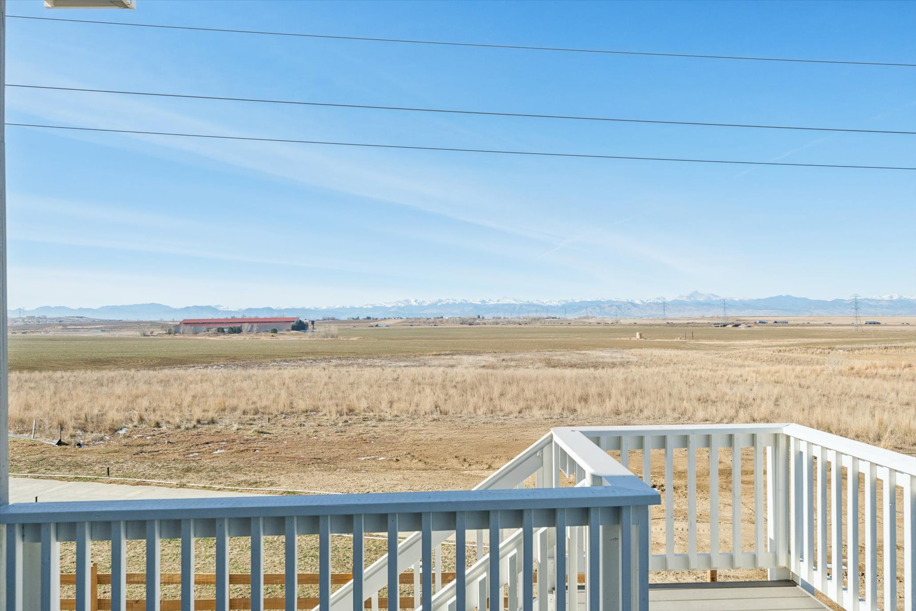 A field with a white fence and a white railing with a red house in the distance.
