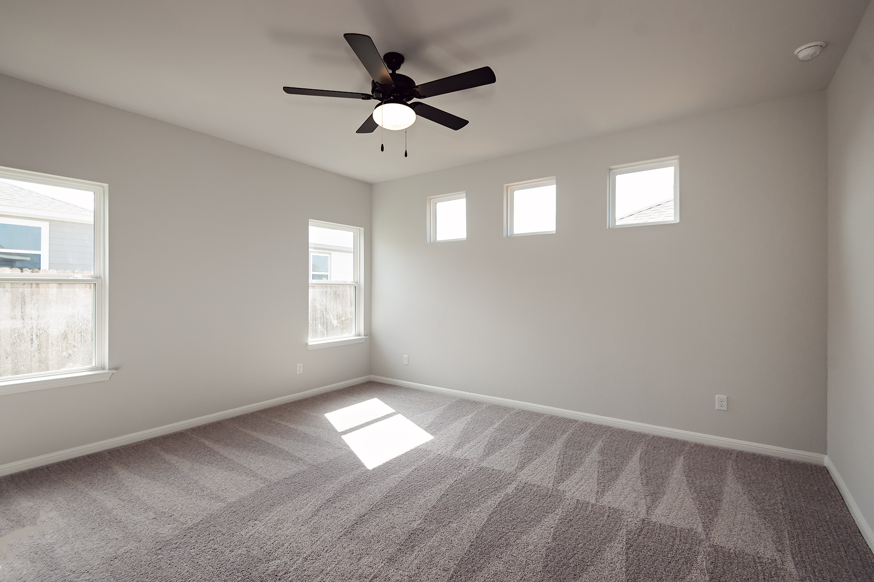 A room with a ceiling fan and a carpet.