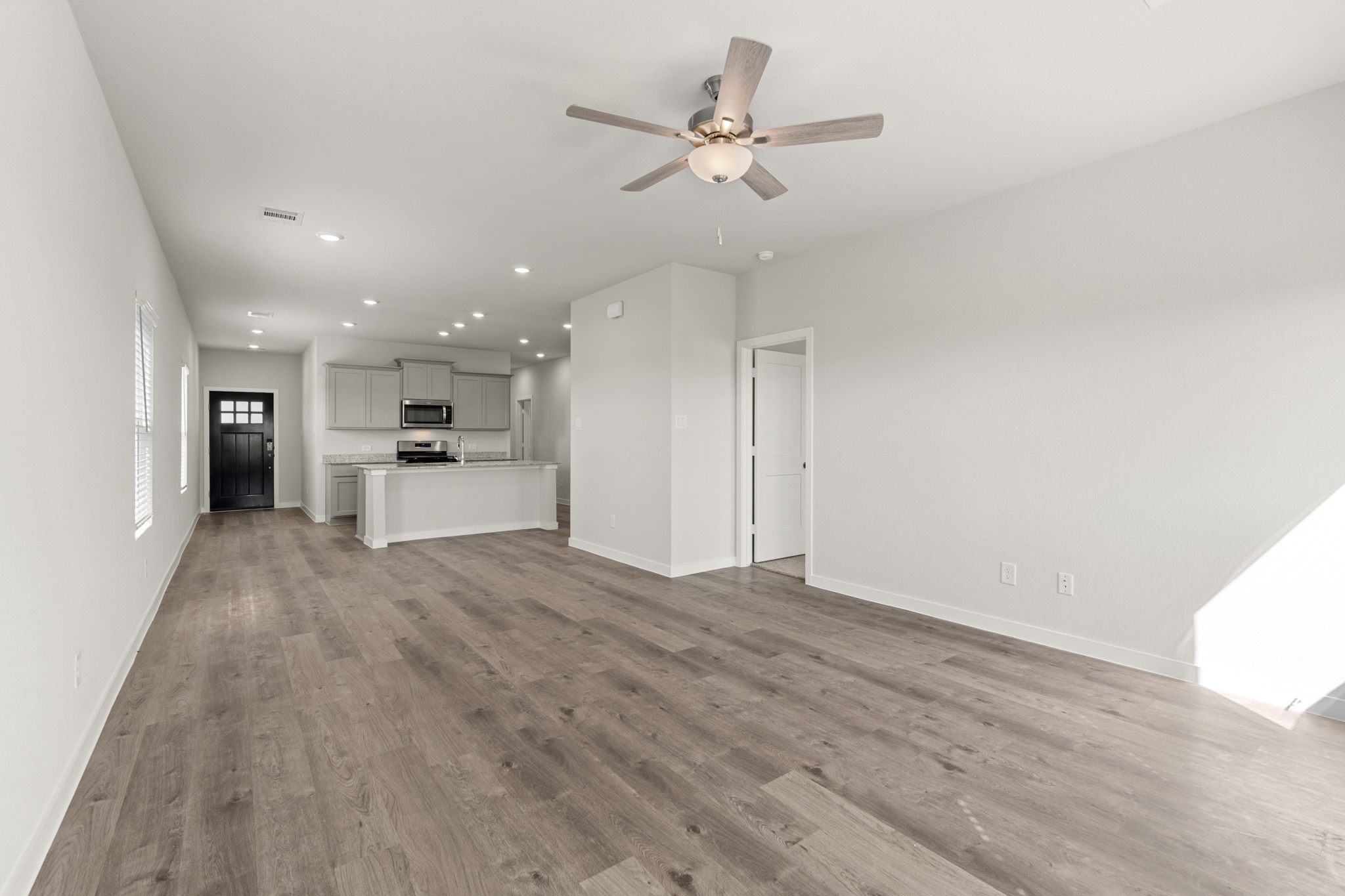 A large empty room with a ceiling fan and a wood floor.
