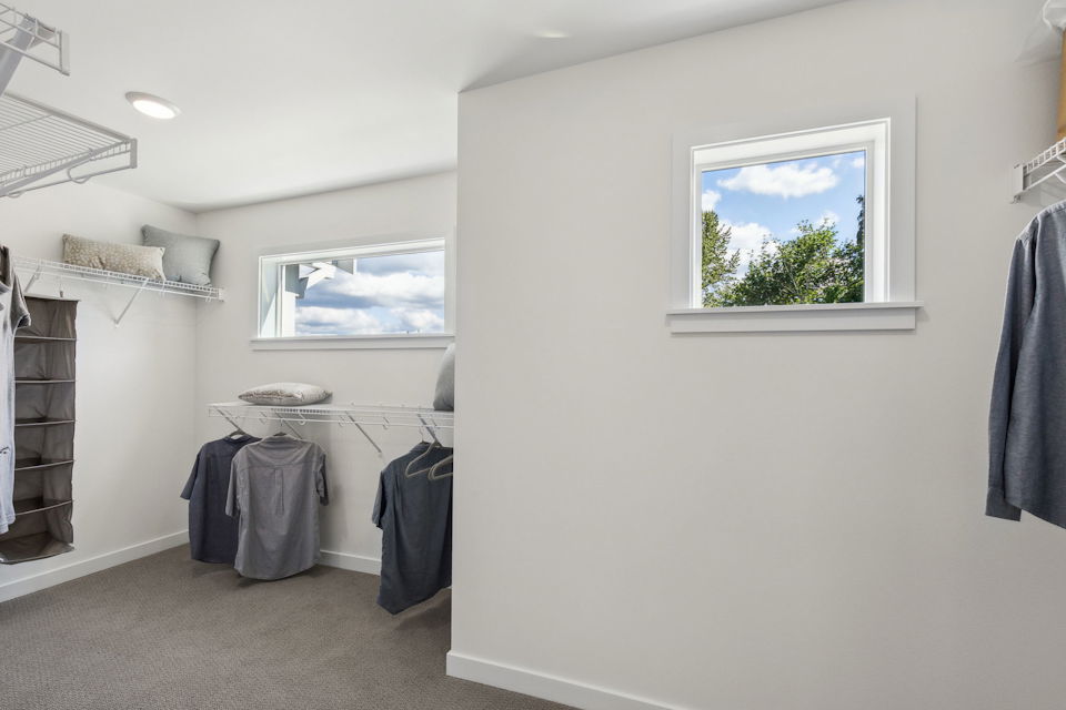 A room with a window and clothes on the wall.